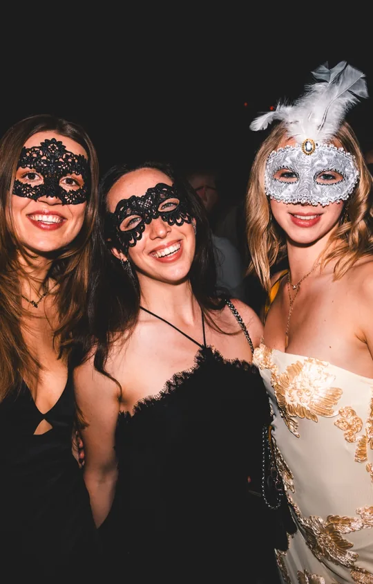 Drei Freundinnen in Abendkleidern mit Spitzenmasken und silberner Federmaske beim Golden Mask, dem Maskenball von Golden Flame in der Flora Köln