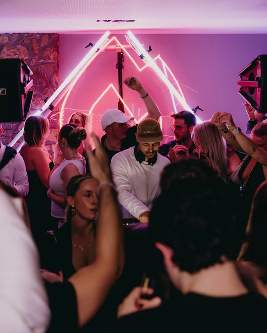 Secret Flame in Köln: tanzende Gäste vor dem DJ-Pult unter dem leuchtenden Neon-Zeichen aus Dreieck und Flamme